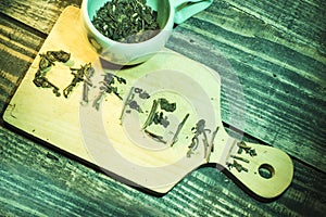 Caffeine words figured by green tea herbs and cup of tea on wooden table