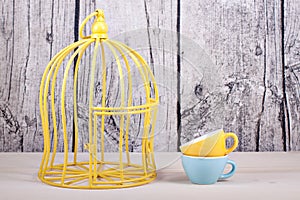 Cage and cups on table over wooden background