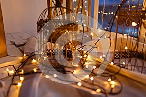 Cages for birds covered with garland with yellow lights. Cozy winter or autumn morning at home. Warm blanket, garland with lights