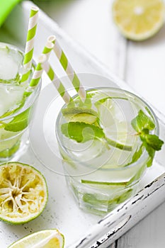 Caipirinha, mojito cocktail with lime, brown sugar, ice and mint leaves in beautiful glasses, cut green citrus on white wooden bac