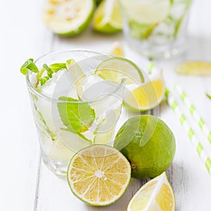 Caipirinha, mojito cocktail with lime, brown sugar, ice and mint leaves in beautiful glasses, cut green citrus on white wooden bac