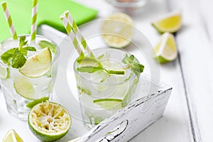 Caipirinha, mojito cocktail with lime, brown sugar, ice and mint leaves in beautiful glasses, cut green citrus on white wooden bac