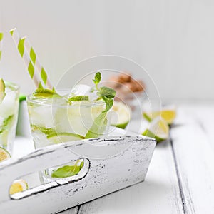 Caipirinha, mojito cocktail with lime, brown sugar, ice and mint leaves in beautiful glasses, cut green citrus on white wooden bac