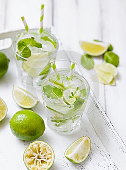 Caipirinha, mojito cocktail with lime, brown sugar, ice and mint leaves in beautiful glasses, cut green citrus on white wooden bac