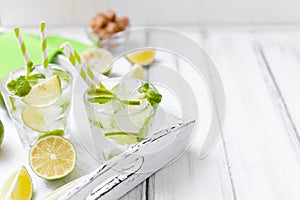 Caipirinha, mojito cocktail with lime, brown sugar, ice and mint leaves in beautiful glasses, cut green citrus on white wooden bac