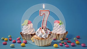 Cake, birthday cupcake with a burning candle number seven, 7 on a blue background.