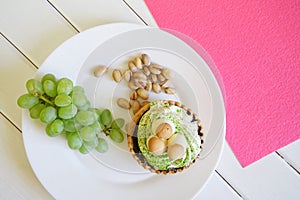 Cake, a bunch of grapes and pistachios in a plate on a white and pink background. Country breakfast