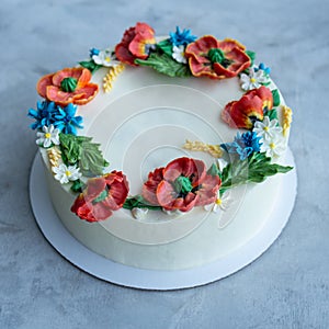 Cake with buttercream frosting decorated with buttercream flowers, Poppies, chamomile, cornflowers, spikelets of wheat, on gray