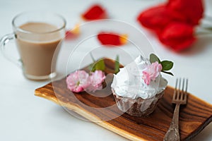Cake and Coffee. Tasty cake with cream and pink flower decor in wooding plate. Red flowers on background