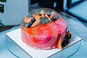 Cake covered in red icing, with strawberries and blueberries.