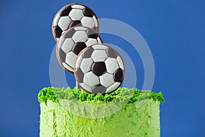 Cake for a football fan with green cream cheese frosting, grass and soccer balls gingerbread cookies on top