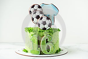 Cake for a football fan with green cream cheese frosting, grass and soccer balls gingerbread cookies on top