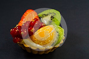 Cake with fresh bio fruit, orange, kiwi, red currant, strawberry, side view photo, black background