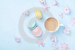 Cake macaron or macaroon, pink flowers and coffee on blue pastel background top view. Creative and fashion composition. Flat lay.