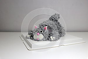 Cake made in the shape of a grey cat. It is doing a crouching pose