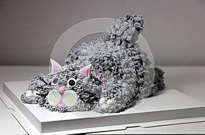Cake made in the shape of a grey cat. It is doing a crouching pose