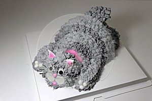 Cake made in the shape of a grey cat with a pink collar. It is doing a crouching pose