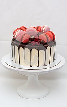 Cake with melted chocolate, red and pink french macaroons, fresh raspberry and chocolate truffles on white cakestand