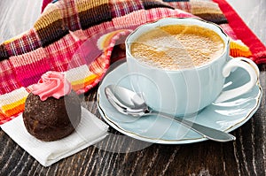 Cake with pink cream on tissue, cup of coffee, spoon on saucer, napkin on table