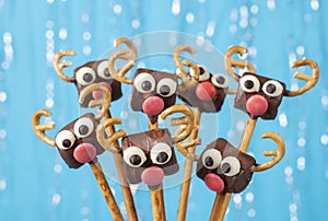 Cake pops Santa reindeers from marshmallows, sweet straw and chocolate on blue background, Idea Christmas treats for