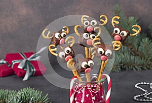 Cake pops Santa reindeers from marshmallows, sweet straw and chocolate on brown background, Idea Christmas treats for