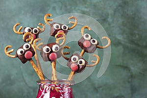 Cake pops Santa reindeers from marshmallows, sweet straw and chocolate on green background, Close up