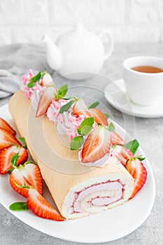 Cake roll with fresh strawberries, jam and cream cheese on a white plate on a gray background. Copy space