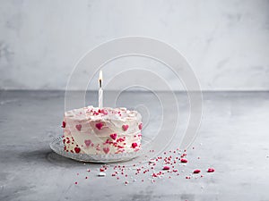 Cake with small hearts and colorful sprinkles with one candle on light background. Romantic love background.