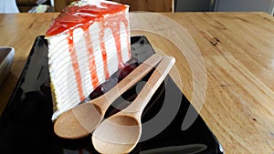 Cake topped with red nectar on a black plate with a wooden spoon placed on the side.