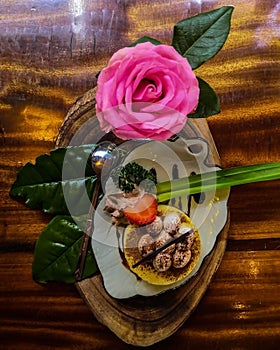 A cake on a tray on a wooden table is a festive breakfast and a pink rose on a wooden table. Top view.