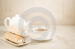 Cake a tubule with white cream and tea cup on a white marble table/ tea drinking with cream cakes on a white marble table.