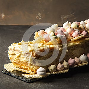 Cake with white chocolate on black table with marshmallows and waffles, home made cake