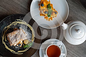 Cakes on plates with tea cup in restaurant, top view