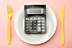 Calculate expensive food spending costs, counting calories and weight loss program concept with calculator onn empty plate, yellow