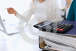 Calculator and binders with papers are waiting to be processed by business woman or bookkeeper working at the desk in