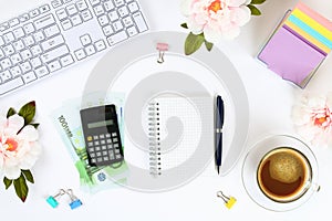 Calculator, euro banknotes, blank notebook on a white desktop next to a coffee mug and a keyboard. Top view, flat layout. Copy the