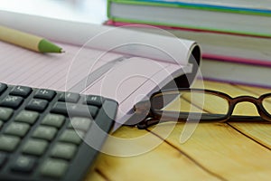 Calculator,eye glasses,pen,receipt and invoice book and stacked of books in the background.