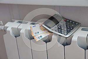 Calculator and fifty euro banknotes lie on the radiator of the heating system, the cost of heat, utility bills.