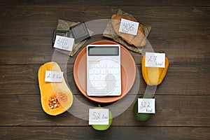 Calculator and food products with calorific value tags on wooden table, flat lay. Weight loss concept photo