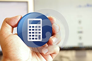 Calculator icon blue round button holding by hand infront of workspace background