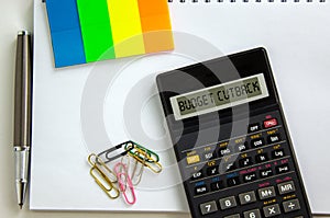 Calculator with inscription `budget cutback`,  white note, colored paper, paper clips, pen. Business concept. Beautiful white