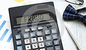 A calculator labeled FRAUD lies on financial documents in the office.