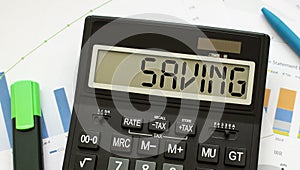 A calculator labeled SAVING lies on financial documents in the office