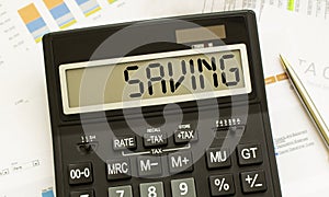 A calculator labeled SAVING lies on financial documents in the office