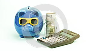 Calculator lies at blue piggy bank and dollar banknotes