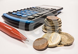 Calculator near a pile of coins and a pen on a white background - business management concept