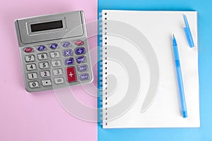 Calculator and notebook with pen on a blue and pink background. stationery