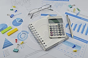 Calculator, notebook, pen, pin and glasses on financial graph, a