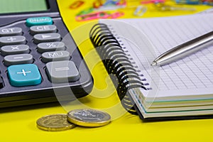 Calculator, notebook and pen on a yellow surface. Side view. Soft focus