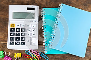 Calculator, notebooks & clips on wooden background